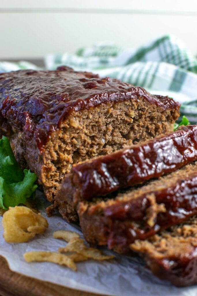 A meatloaf glazed on a wood platter with a few slices cut away from the end.