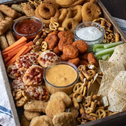 A snack board made for game day featuring all the foods found at a sports bar such as nachos, wings and pizza.