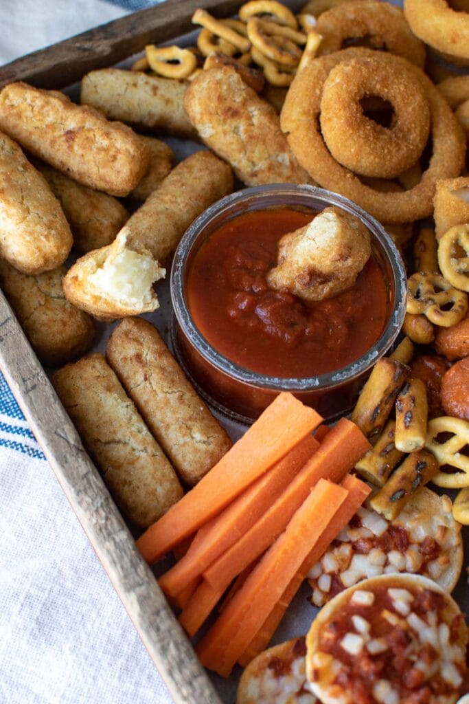 A game day appetizer platter with mozzarella sticks, marinara sauce, onion rings, and carrot sticks.
