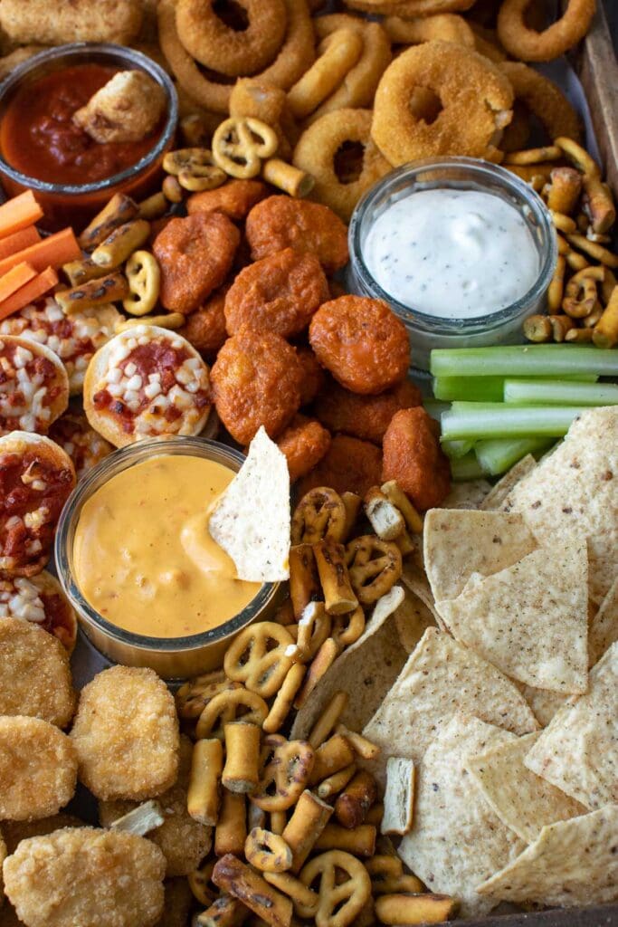 A game day charcuterie board full of chicken wings, mini pizzas, nachos, and pretzels.