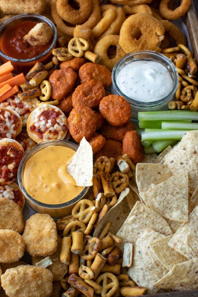 A game day charcuterie board full of chicken wings, mini pizzas, nachos, and pretzels.