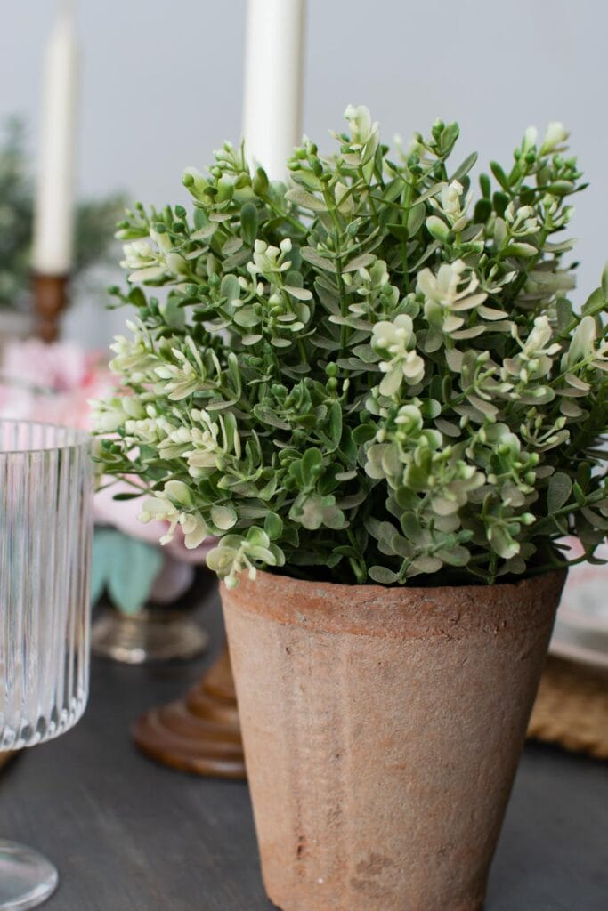 A faux green plant in a rustic clay pot.