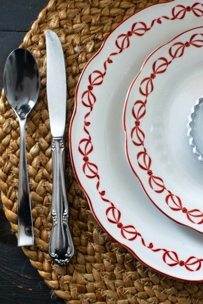 Mix-matched silverware beside white plates with little red bows along the edges.