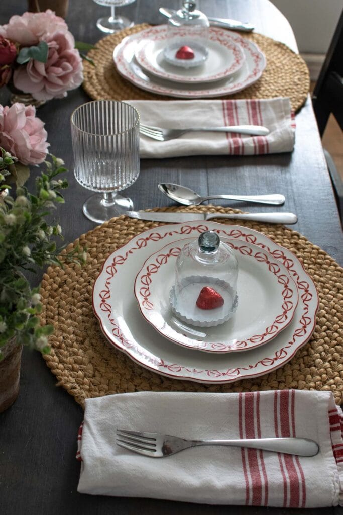 Valentine's table setting using white plates with red bows, chocolate hearts in red foil and natural seagrass placemats.