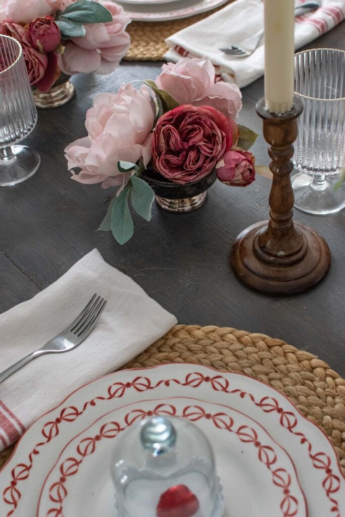 A Valentine's Day table set for four, include white plates with red bows around the edge, a small cloche with a chocolate heart in the centre on top of each plate.