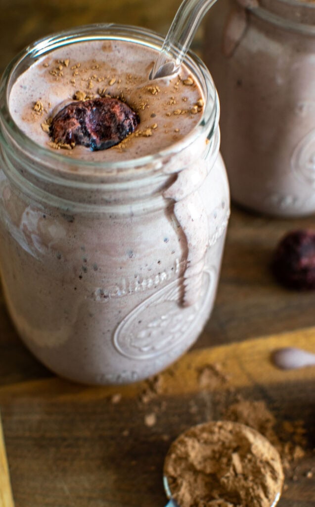 A Black Forest smoothie in a mason jar, topped with a frozen sweet cherry and cocoa powder.