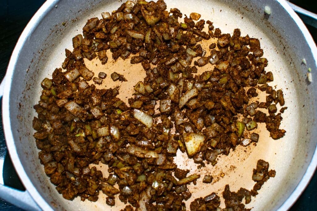 Chili powder, cumin and chopped onions mixed together in a frying pan.