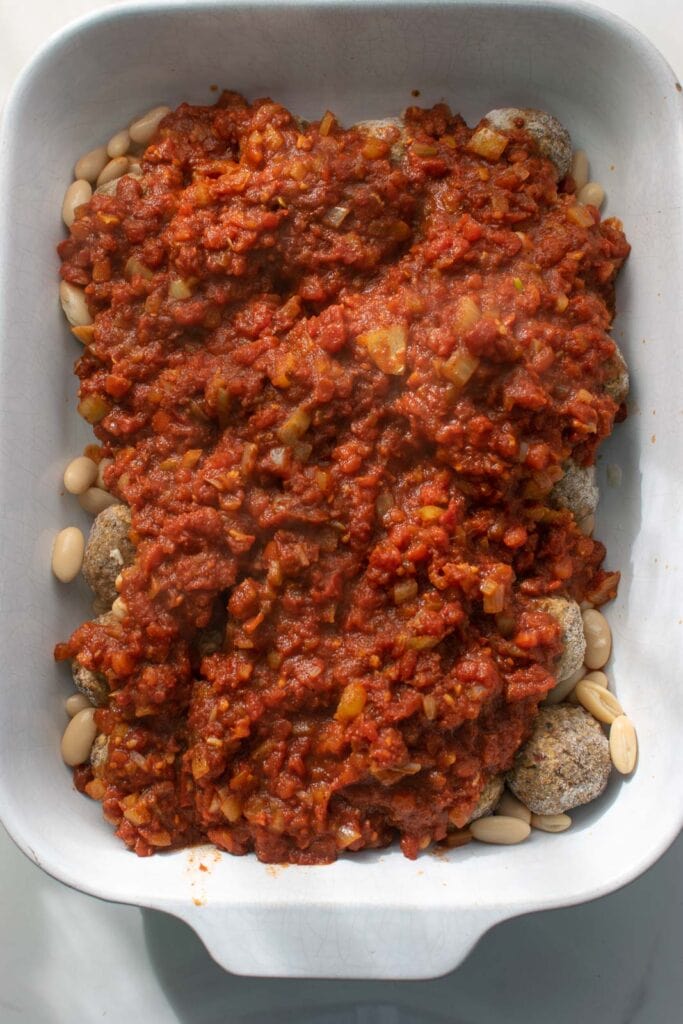 Tomato chili powder mixture poured over frozen meatballs and kidney beans in a casserole dish.