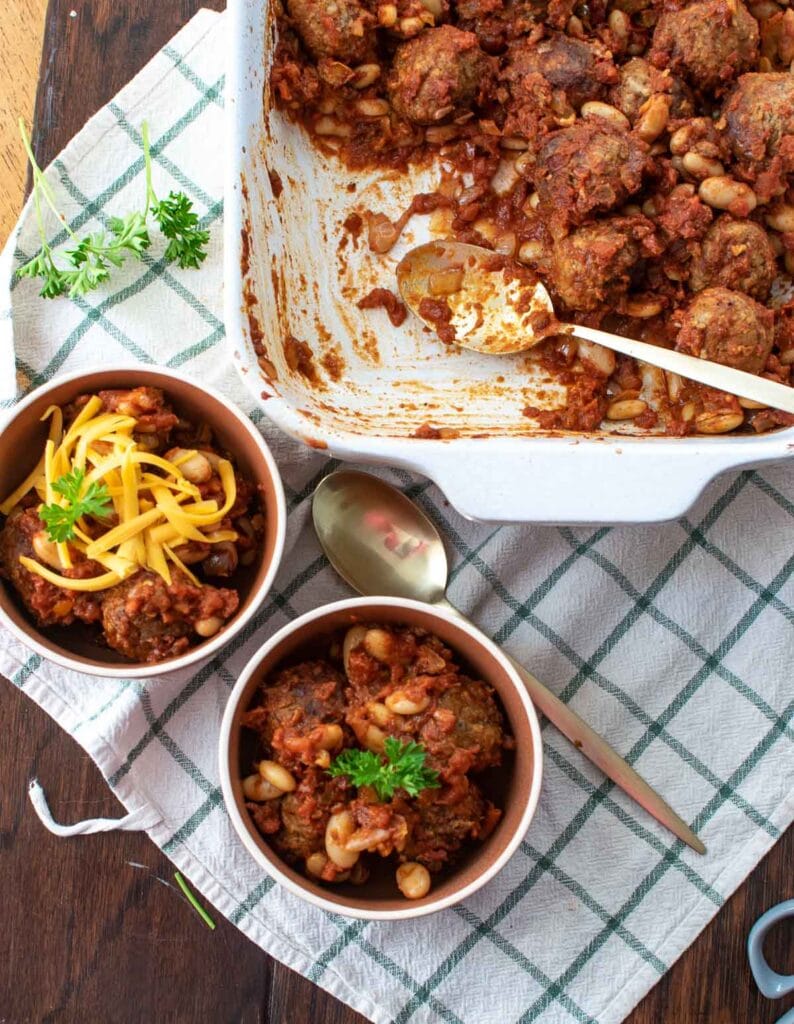 Two bowls of meatball chili beside the casserole dish it came from.