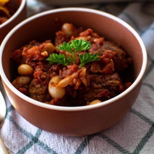 A small bowl of oven baked meatball chili casserole on a white plaid kitchen towel.