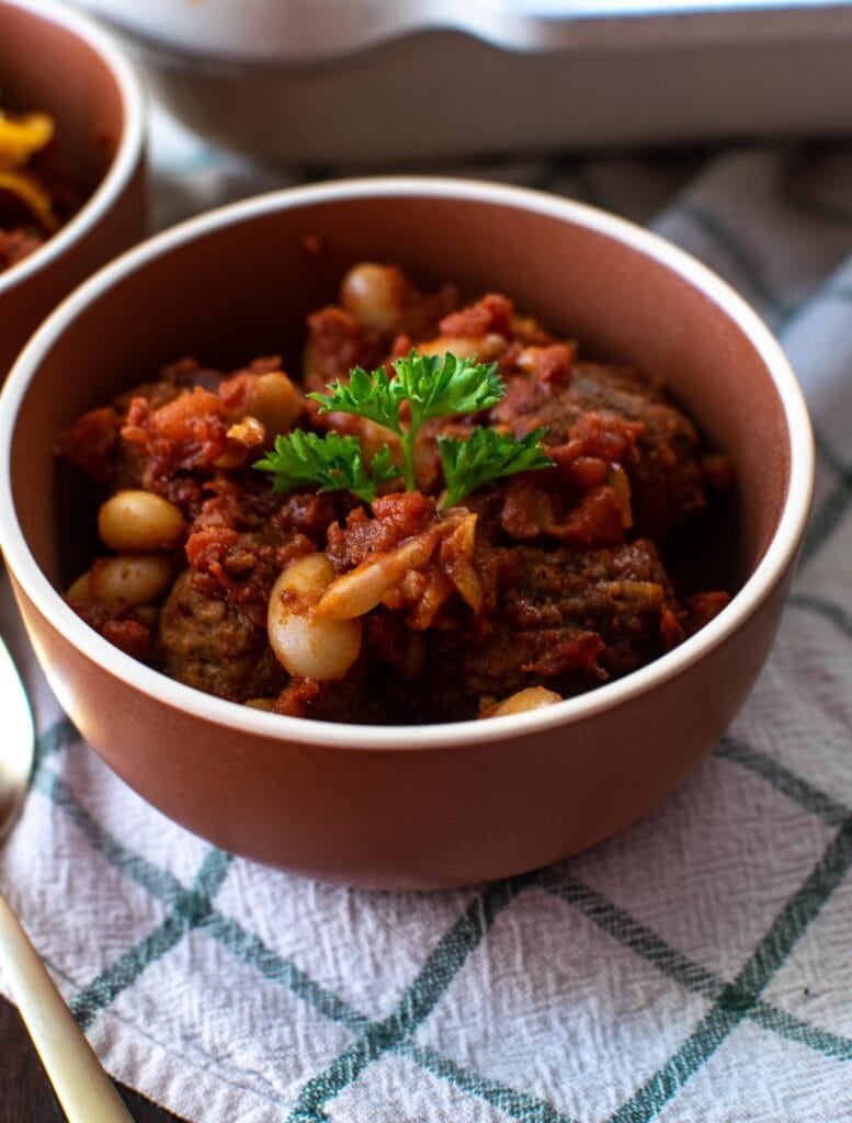 A small bowl of oven baked meatball chili casserole on a white plaid kitchen towel.
