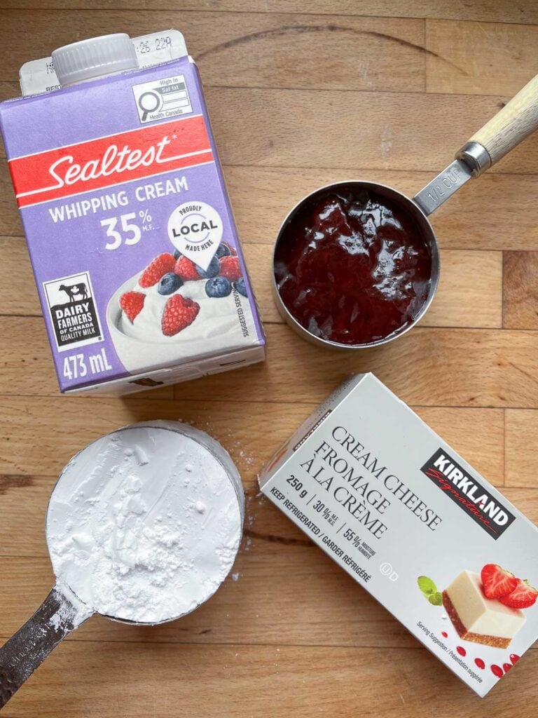 Ingredients to make strawberry cream cheese mousse including cream cheese, icing sugar, whipping cream and strawberry jam.
