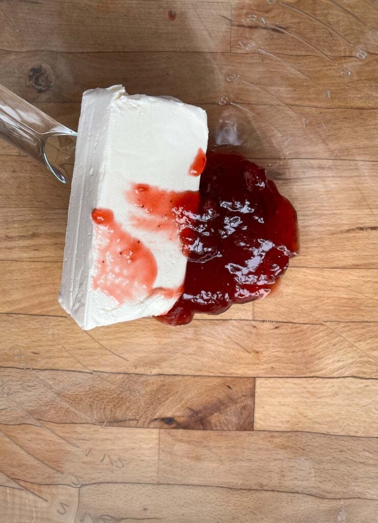 A block of regular cream cheese and a half cup of strawberry jam in the bowl of an electric mixer.