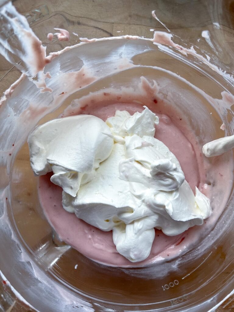 Freshly whipped cream added to a bowl with a strawberry cream cheese mixture.