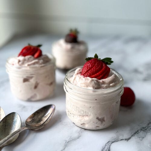 3 small Mason jars filled with strawberry cream cheese mousse and topped with fresh strawberries.