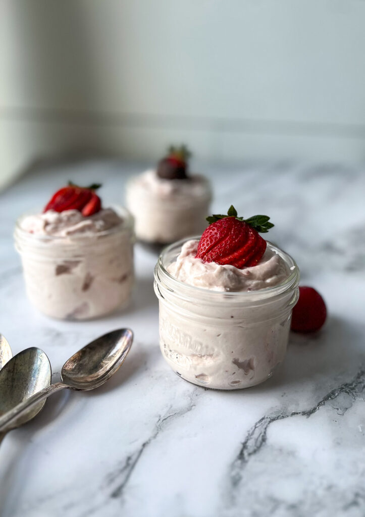 3 small Mason jars filled with strawberry cream cheese mousse and topped with fresh strawberries.