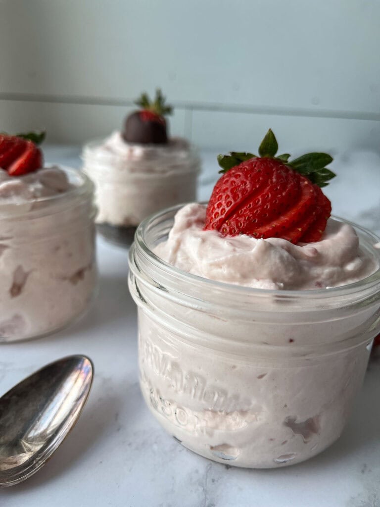 Three small Mason jars with strawberry mousse and topped with fresh sliced strawberries.