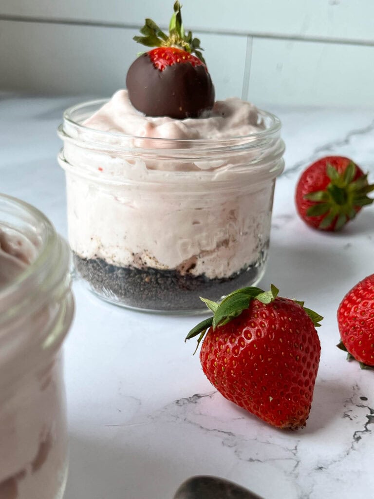 Strawberry mousse in a small jar with a layer of chocolate cookie crumbs on the bottom and a chocolate covered strawberry on top.