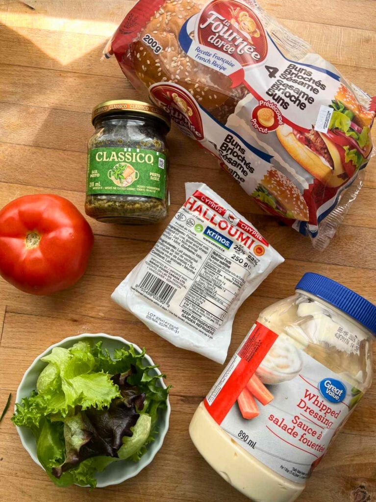 Ingredients to make a Halloumi sandwich including whipped salad dressing, pesto, tomato, lettuce and brioche buns.