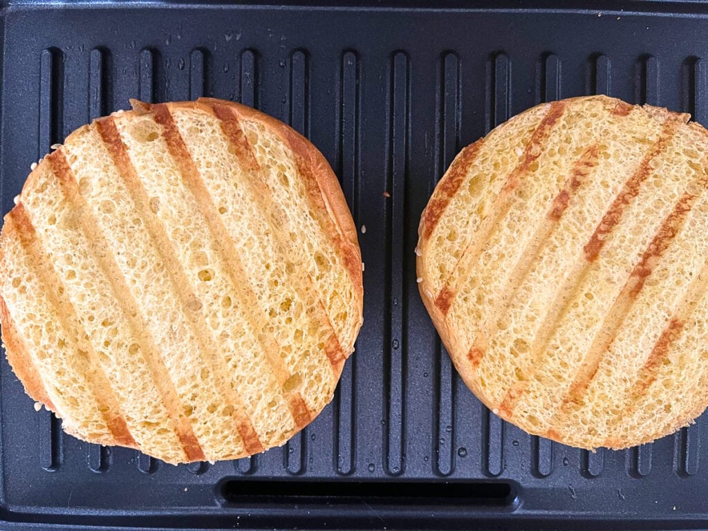 The outside of a split brioche bun toasted on a grill.