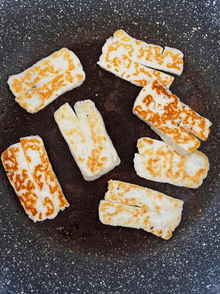 Halloumi cheese frying pan that has just been flipped to cook the other side. The browned, crispy side is showing.