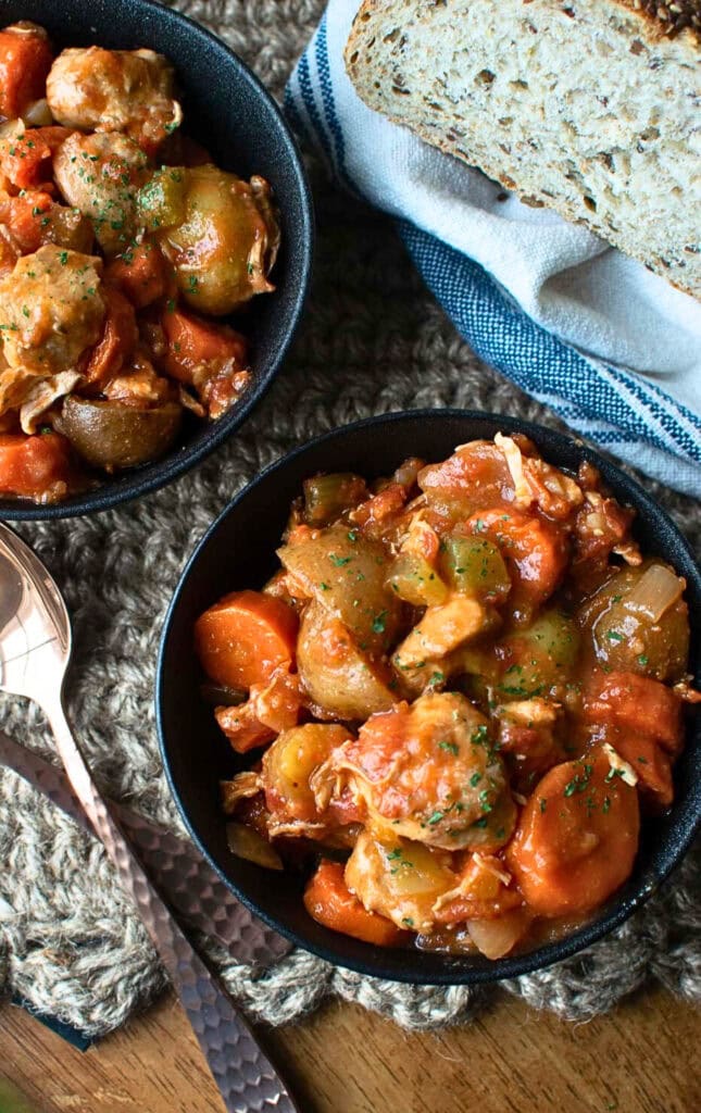 Two bowls of chicken and vegetable stew with a loaf of sour dough bread to the side.