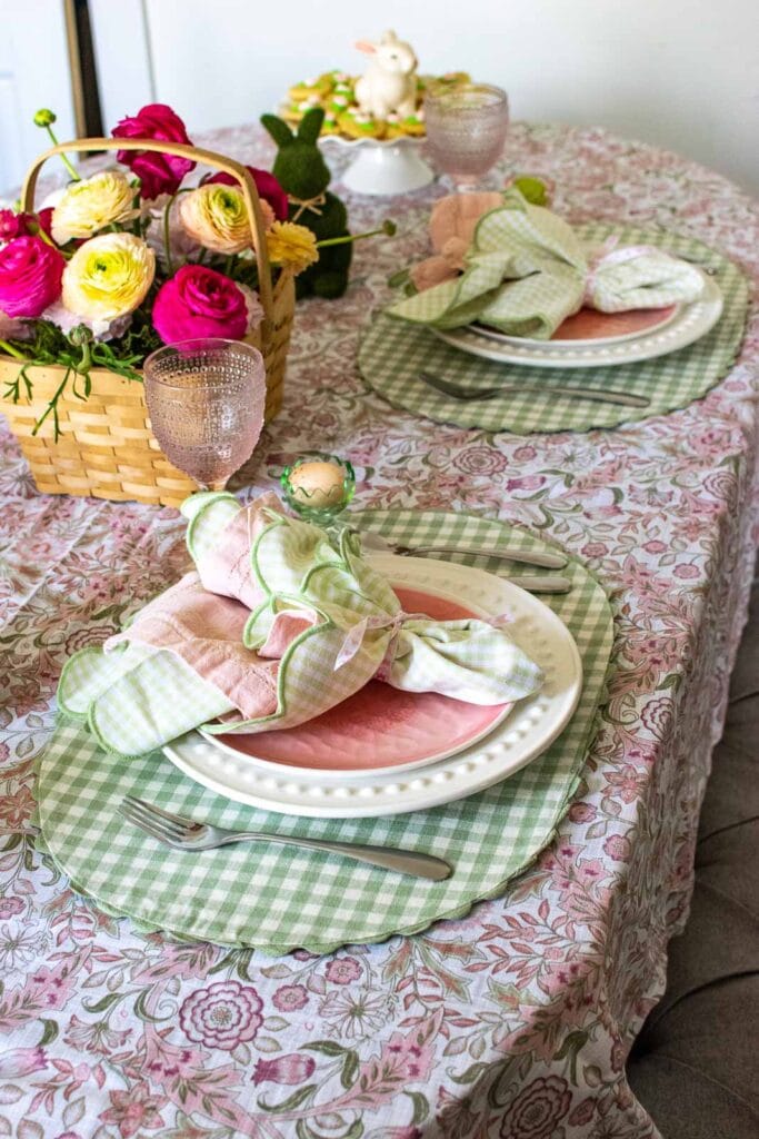 A pink and green tablecloth with green gingham placemats, a ranunculus centrepiece in a wicker basket.
