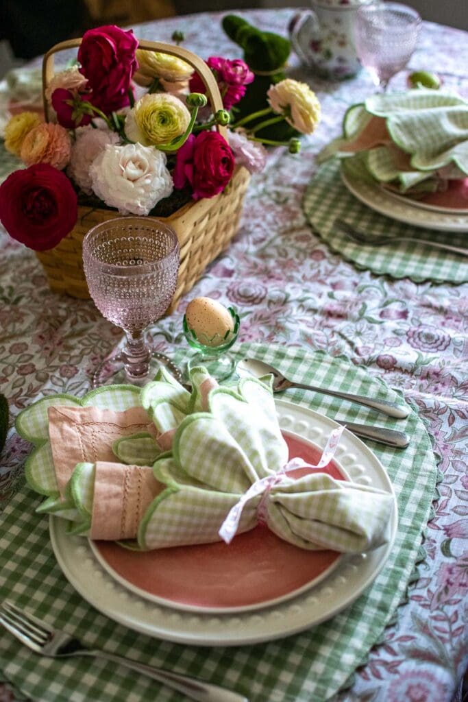 An Easter table place setting with gingham napkins, pink glassware and a green glass egg cup.