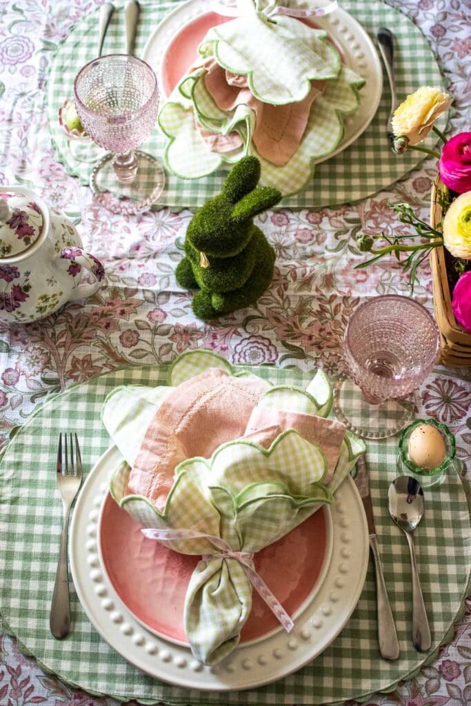 A table set for Easter with a moss covered bunny, pink and white plates, a teapot and pink glassware.