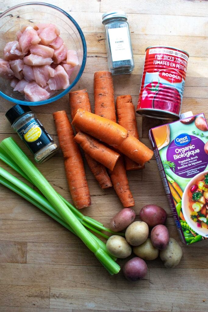 Ingredients to make slow cooker chicken stew including carrots celery, onions, potatoes, chicken and broth.