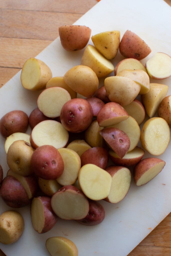 Mini red and white potatoes cut into halves on a cutting board.