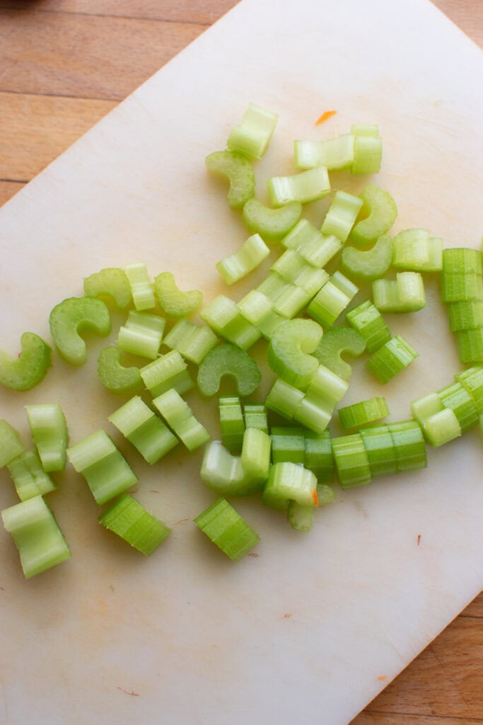 Three ribs of celery cut into half inch pieces on a cutting board.