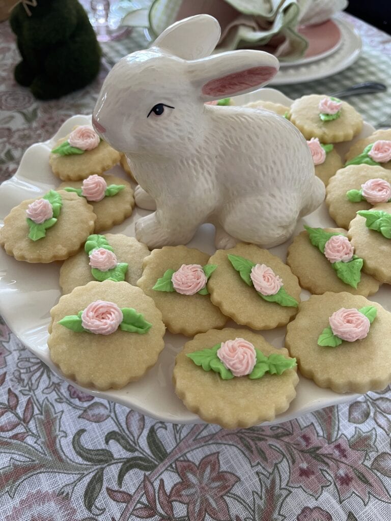 A plate of round shortbread cookies decorated with green leaves and pink flowers.