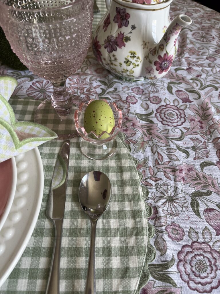 A pink and green patterned William Morris table cloth topped with green gingham placemats with rickrack trim.