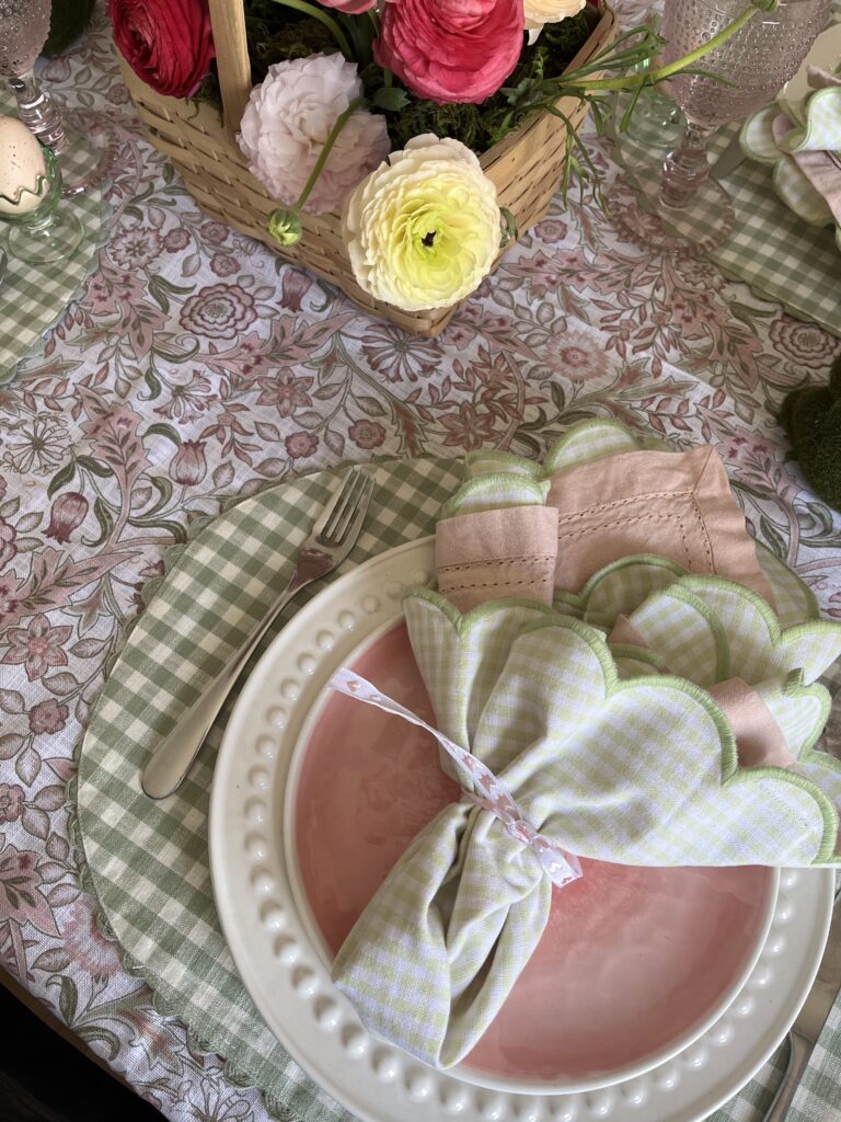 A table set for Easter with a green and pink floral tablecloth and green gingham place mats and napkins.