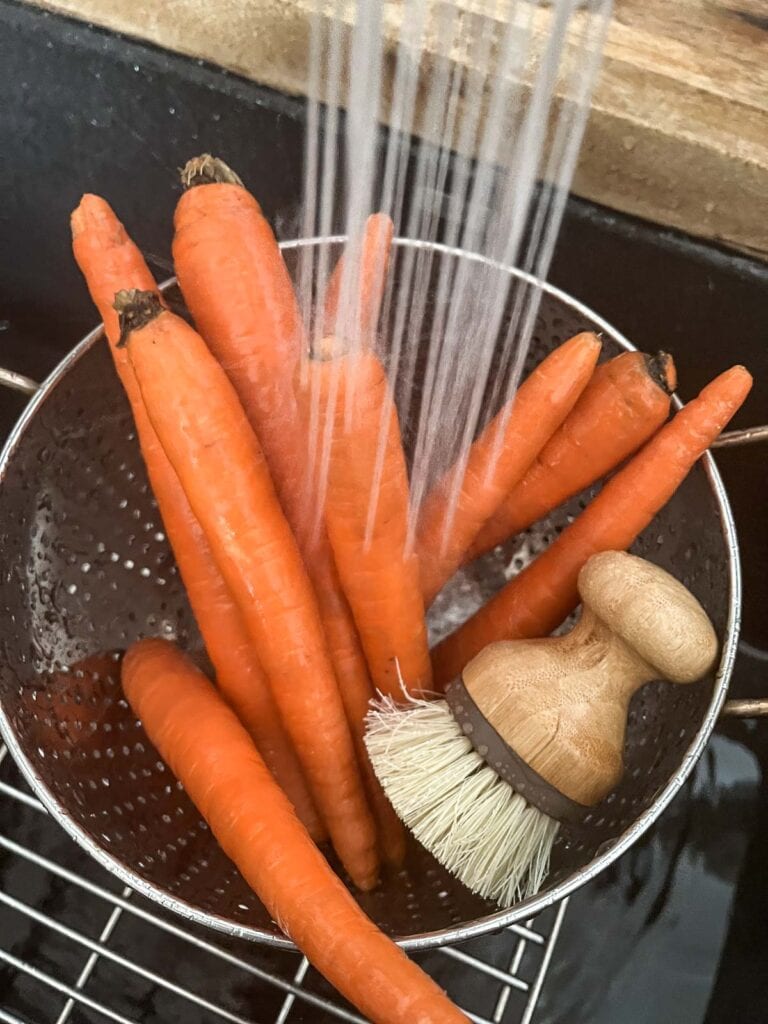 Fresh carrots being washed in a colander in the sink.