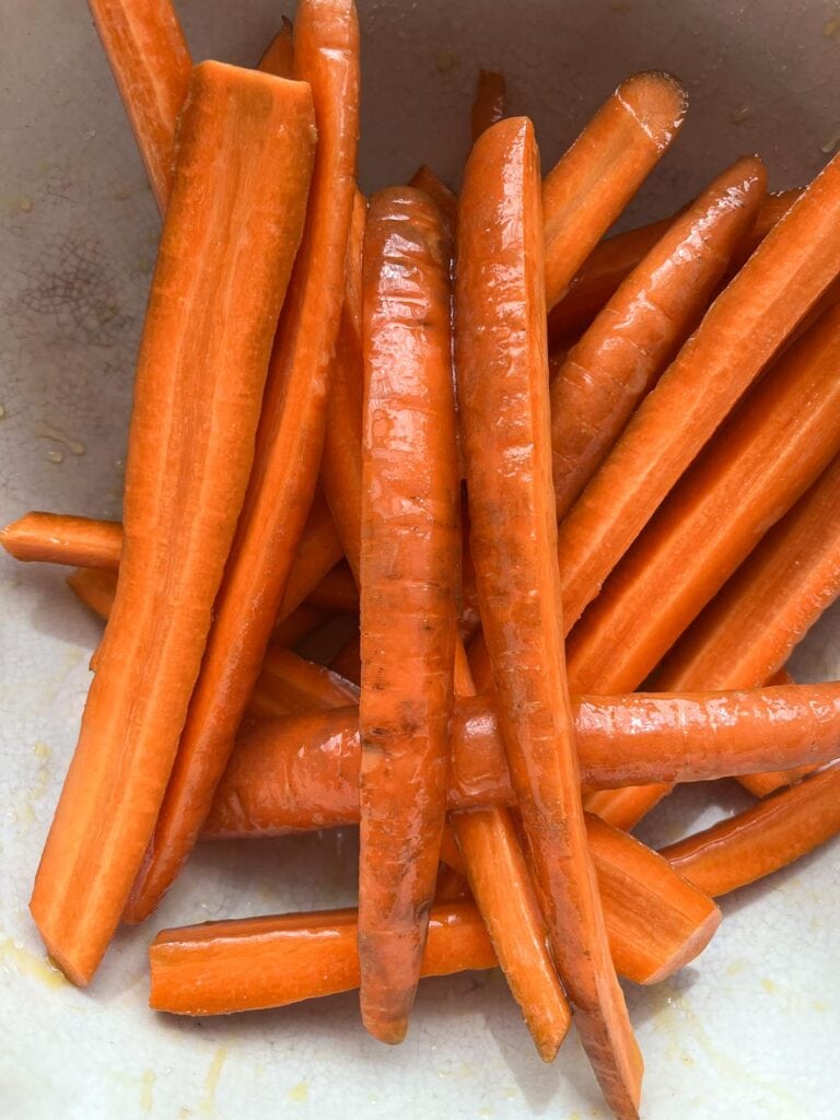 Carrots in a mixing bowl tossed with olive oil, honey and orange juice.