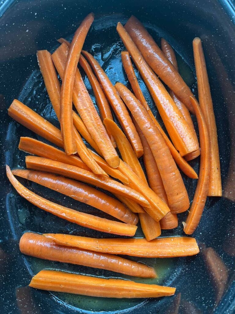 Carrots tossed with olive oil, honey and orange juice placed into a preheated roasting pan.