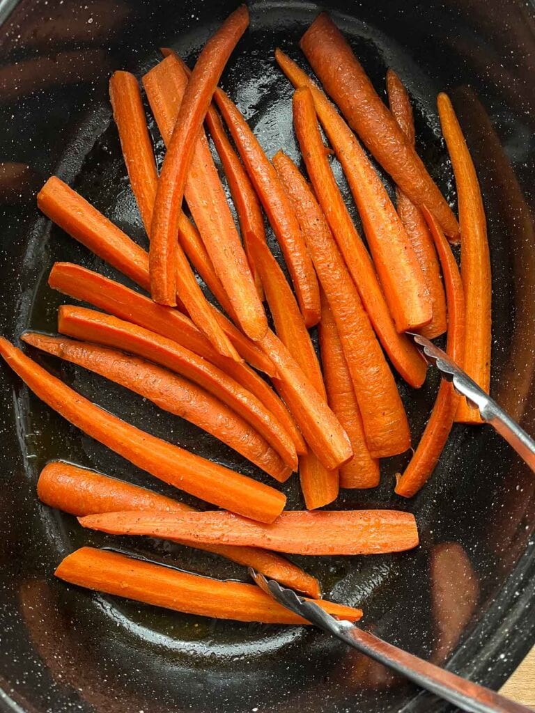 Carrots in a roasting pan brought out of the oven half way through cooking so they can be turned.