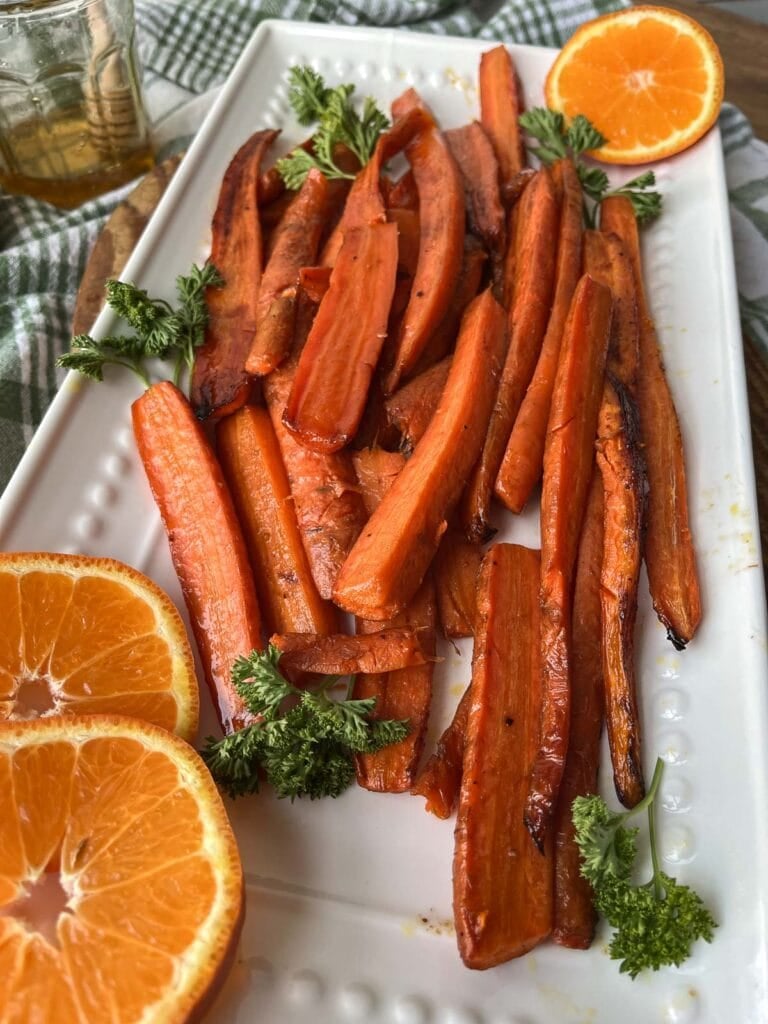 Roasted glazed carrots on a white serving tray and garnished with fresh parsley and orange slices.