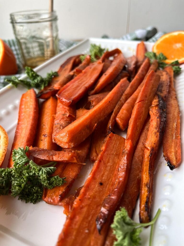Orange Honey Glazed Carrots on a white serving platter garnished with fresh orange slices.