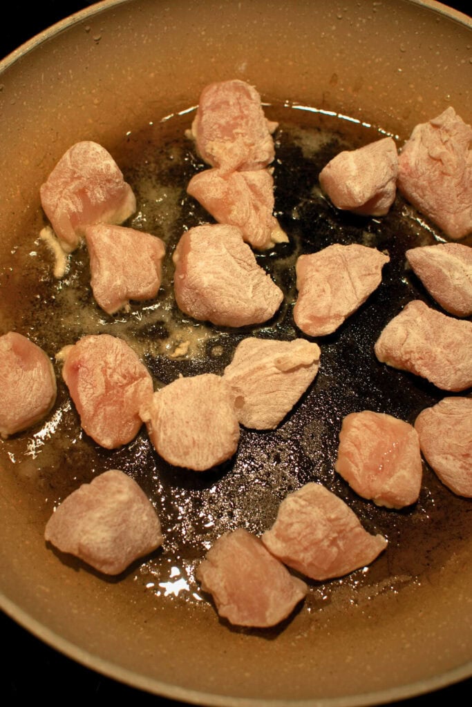 Chicken pieces coated with flour being seared in the frying pan on the stove.