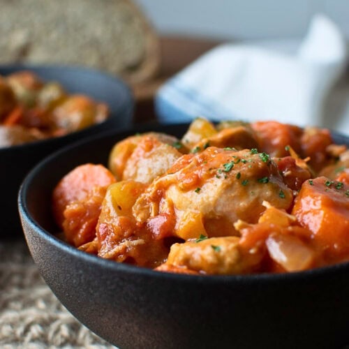 A bowl of chicken and vegetable stew in a black ceramic bowl.