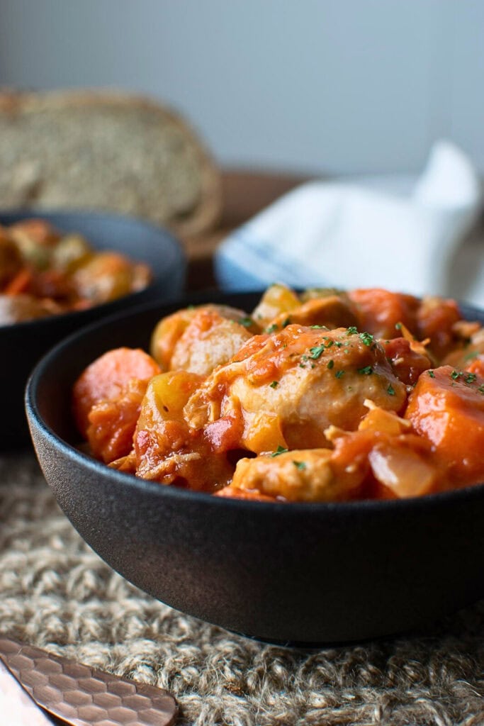 A bowl of chicken and vegetable stew in a black ceramic bowl.