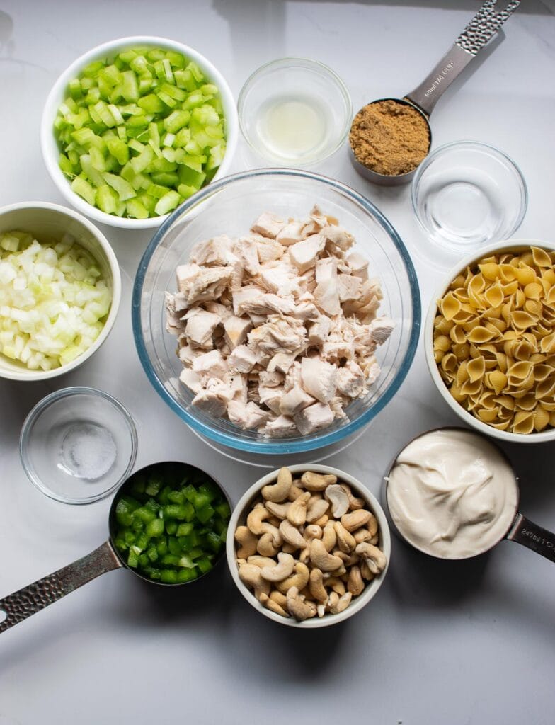 All the ingredients measured out to make cashew chicken pasta salad including chicken, pasta, green pepper, celery, onion and mayonnaise.