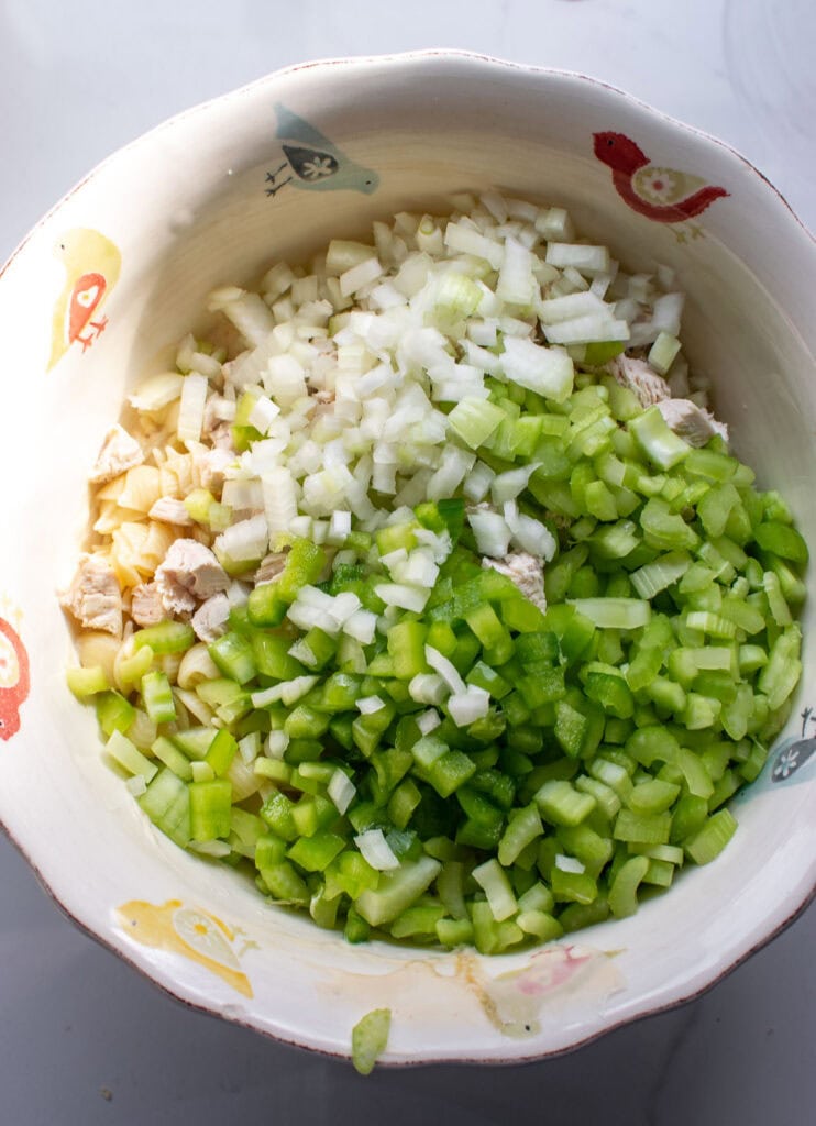 Cooked shell macaroni, chopped green peppers, onions, and chopped chicken breast added into the bowl with the mayonnaise mixture before stirring together.