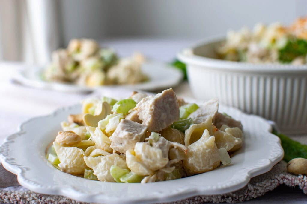A plate of cashew chicken pasta salad on a plate with scalloped edges.