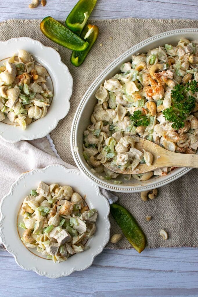 A serving bowl of chicken pasta salad with some scooped out onto two salad plates.