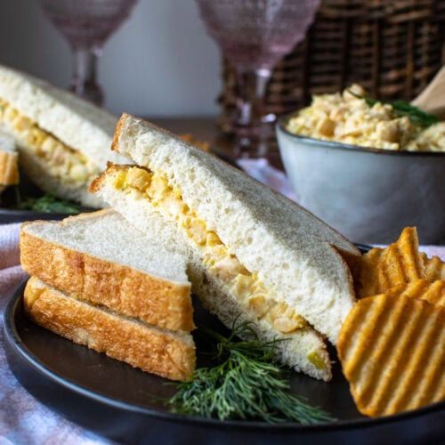 A dill chickpea salad sandwich sliced in half with a side of potato chips.