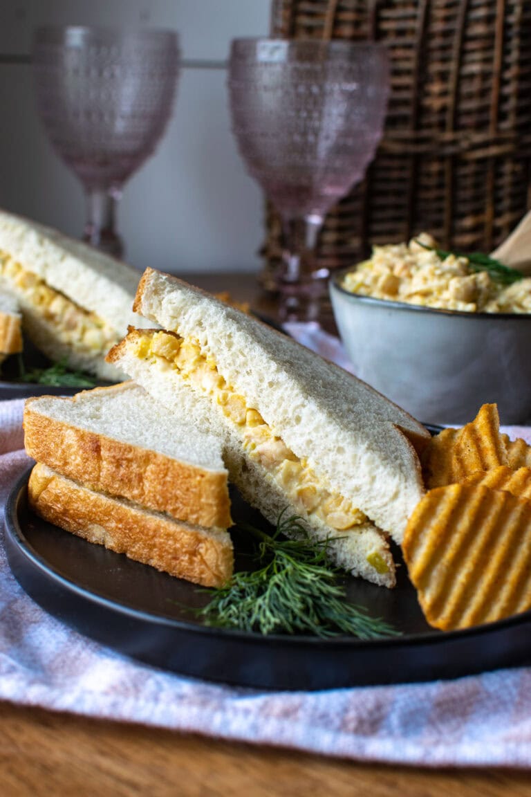 A dill chickpea salad sandwich sliced in half with a side of potato chips.